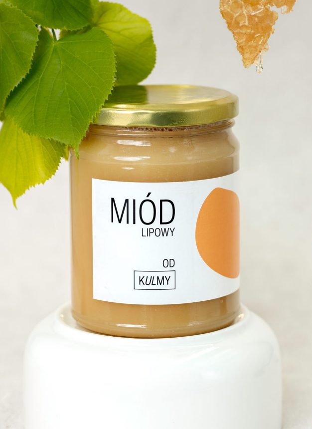 Miód lipowy na jasnej podstawce z liśćmi i plastrem miodu.